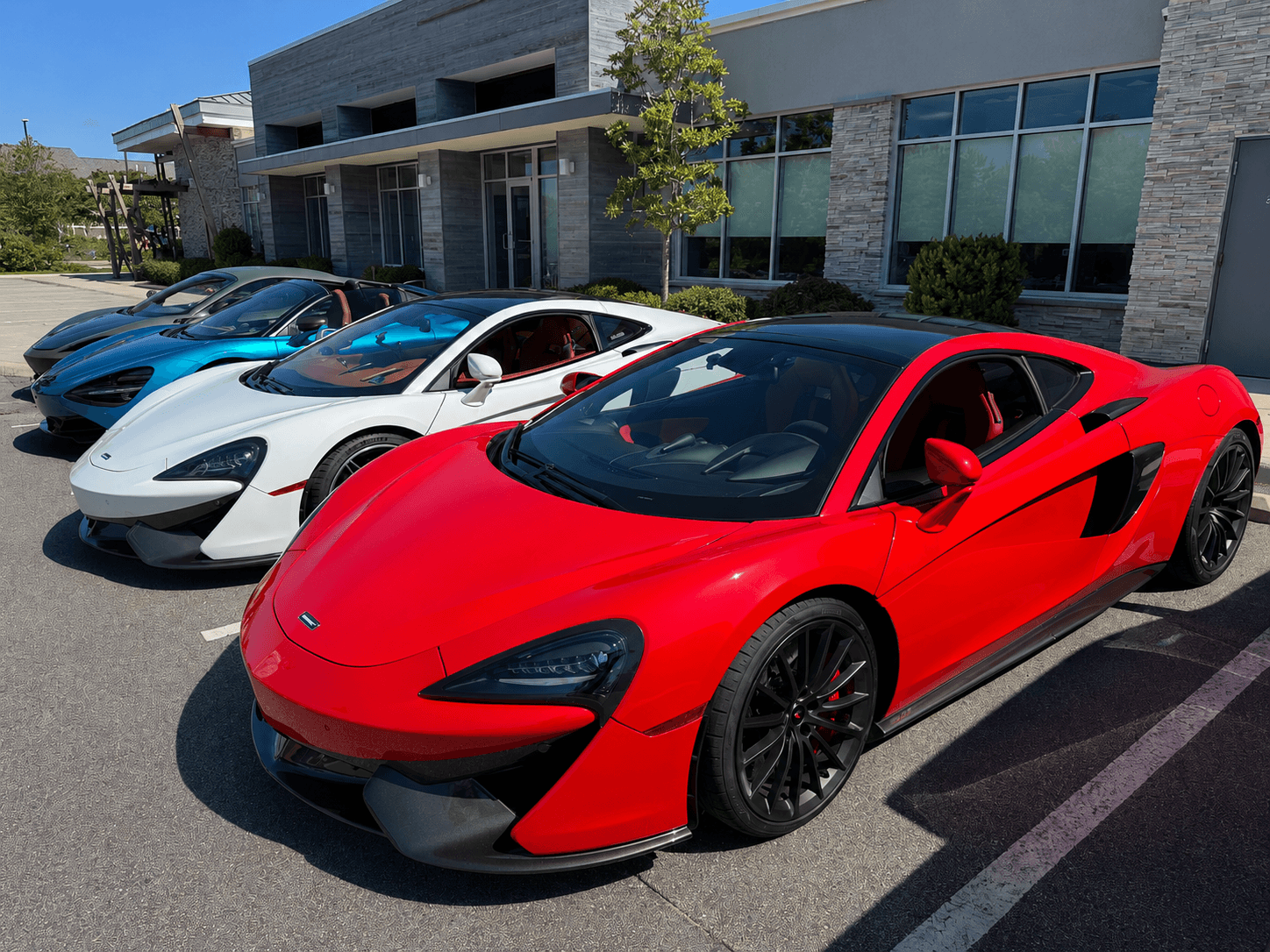 A red McLaren parked alongside white and blue McLarens at a Cars & Coffee event