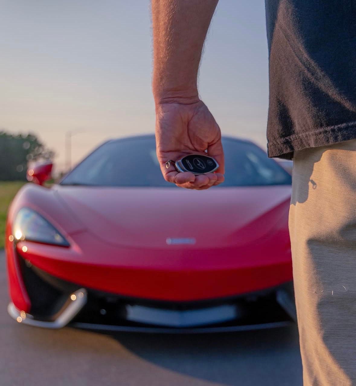 A McLaren key held in front of an exotic car